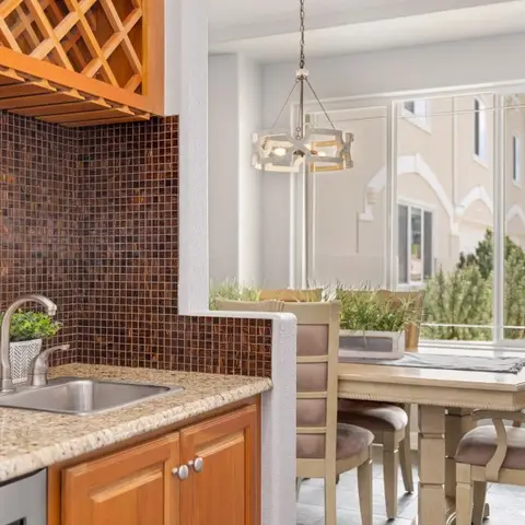 Wet bar with a mosaic-tile backsplash and built-in wine rack opening onto a sunlit dining nook with a wrought-iron chandelier.