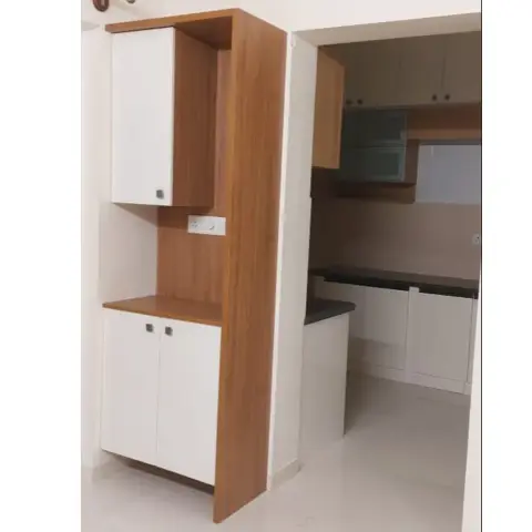 White-and-teak laminate crockery unit with an open appliance niche and a socket, standing at the doorway of an empty parallel modular kitchen with black
