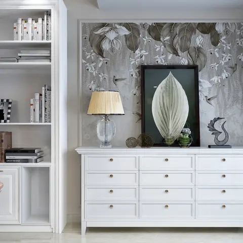 White built-in bookshelf beside a chest of drawers dressed with a botanical mural wallpaper panel and a styled tabletop vignette