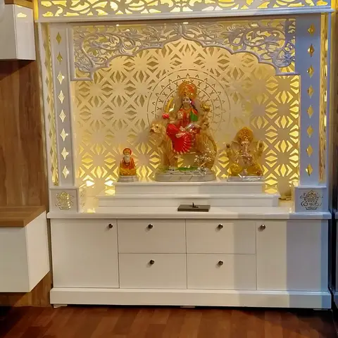 White CNC-jaali pooja unit with a domed pediment and backlit gold jaali panel housing deity idols, over a storage cabinet base on a wood floor.