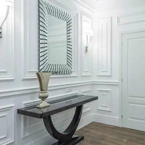 White entrance foyer with full-height raised panel wall moulding, wall sconces flanking a sunburst-frame mirror
