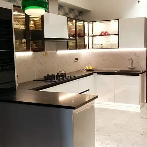 White gloss L-shaped kitchen with black granite counters, marble-pattern backsplash and a green pendant over the peninsula.