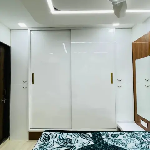 White gloss sliding wardrobe wall with slim brass flush pulls and drawer banks on both flanks, next to a walnut-framed dressing mirror