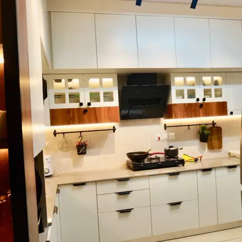 White handleless kitchen with walnut accent bands under the glass wall cabinets, an LED strip washing the beige stacked-tile dado