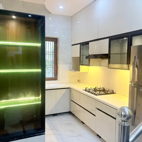 White high-gloss handleless kitchen with black-glass upper cabinets and warm under-cabinet lighting, marble-look counter and wall cladding