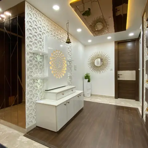 White high-gloss pooja unit on a dark wood-finish platform, a gold Om mandala backlit between CNC-cut jaali screens