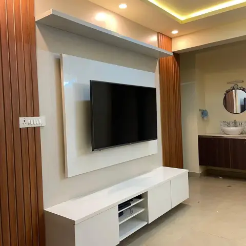 White high-gloss TV console below a wood-fluted panelling wall with cove-lit ceiling, opening onto a wash-basin counter alcove in the background