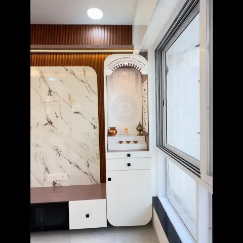 White jaali-arch pooja unit with an Om motif backdrop and brass kalash, set against a marble feature wall and fluted wood panelling.