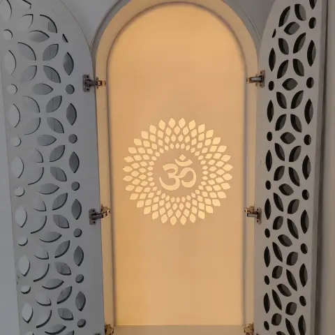 White jaali-pattern pooja unit with an arched niche backlit around a cutout Om motif, doors open, drawer below.