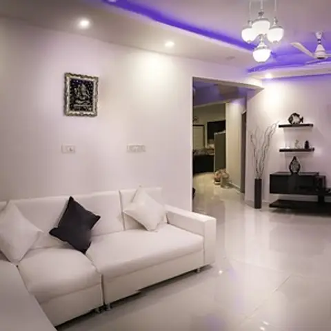 White L-shaped sofa living room with black and white cushions, a cube-shelf TV unit, and a stepped ceiling lit with purple cove lighting