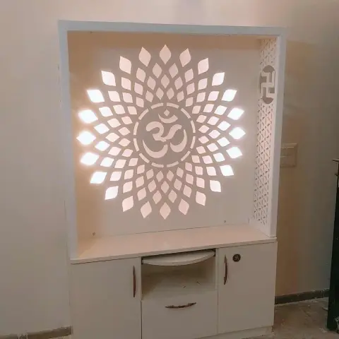 White laminate pooja unit with a backlit Om jaali panel radiating from a lotus-petal cutout, and swastik-motif drawer handles.