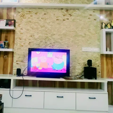 White laminate TV console with open display cubbies below a stacked-stone and wood cladding feature wall