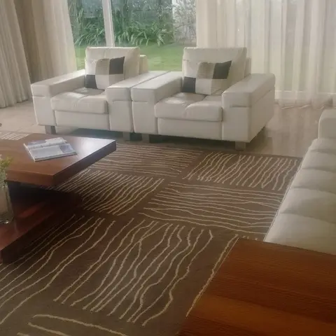 White leather sofa and armchairs around layered wood coffee tables in a glass-walled living room facing a garden.