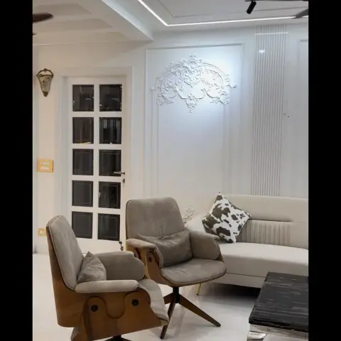 White living room with a curved cream sofa, wood-frame swivel armchairs, a marble-top coffee table, and an ornate plaster relief above a black-grid glazed door.