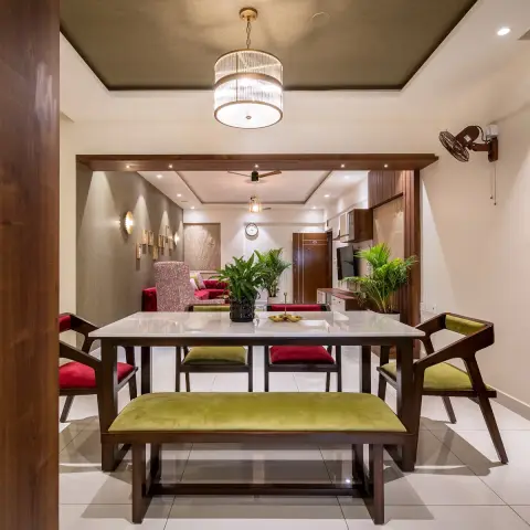 White marble-top dining table framed head-on, with an olive velvet bench, alternating olive and red velvet armchairs