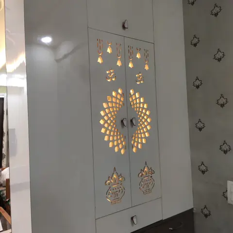 White pooja unit with backlit gold CNC-cut jaali doors featuring Om symbols, temple bells and kalash motifs in a radial mandala pattern