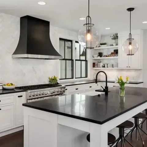 White shaker kitchen with a black flared range hood over a stainless range, a honed black island top with matte-black gooseneck tap and two clear glass globe
