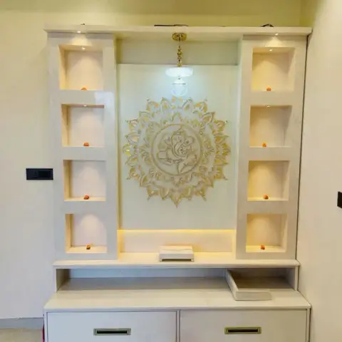 White stone-clad mandir with two columns of backlit square niches flanking a gold-finished carved Ganesha mandala