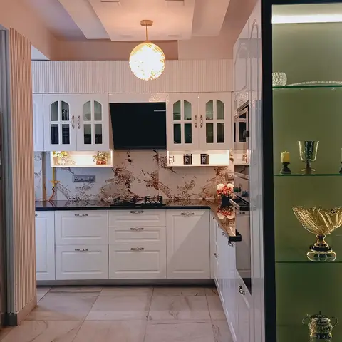 White traditional kitchen with lattice glass-front cabinets, a veined marble backsplash and black granite counters