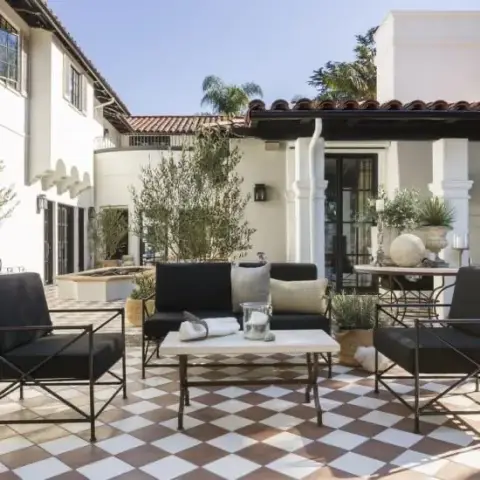 Whitewashed courtyard terrace floored in a red-and-cream diagonal checkerboard tile, with black-cushioned wrought-iron armchairs and a low stone-topped table