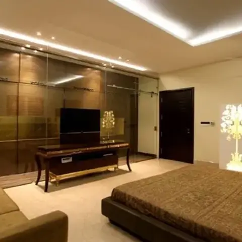 Wide bedroom with a full-height bronze-tinted glass sliding wardrobe wall, a wall TV over a carved wooden console