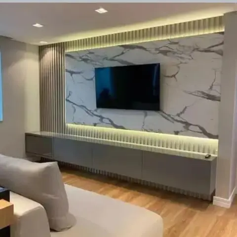 Wide living-room TV wall in grey-veined marble framed above and below by backlit fluted bands