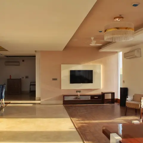 Wide living room where a dark timber-floored seating island with Jeanneret-style strap armchairs steps out of beige stone flooring