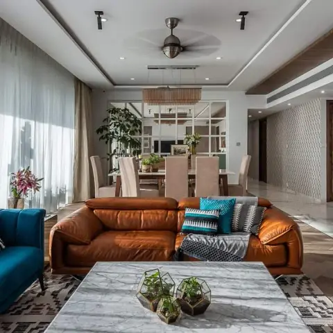 Wide open-plan living room with a tan leather recliner sofa facing a teal velvet couch across a thick white-marble coffee table