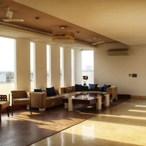 Wide top-floor living room where afternoon sun through a run of six tall slot windows stripes a beige marble floor bordered in dark wood