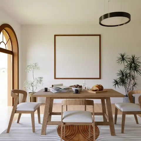 Wood dining table and bench under a round black drum pendant light, beside an arched wood-framed door and a blank frame mockup on the wall.