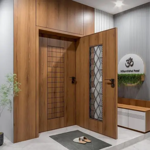 Wood-finish main door with a laser-cut jaali insert opening into a foyer with an Om nameplate and a white-shuttered shoe console.