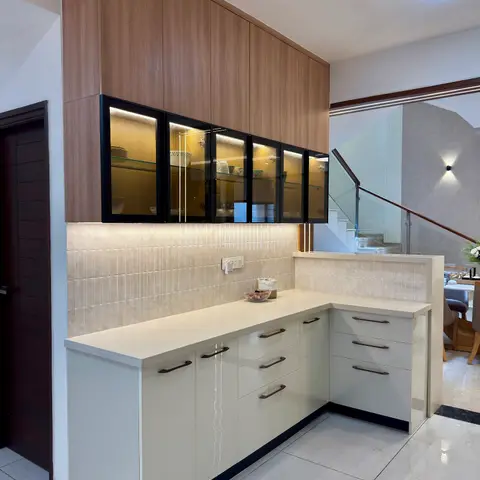 Wood-finish overhead crockery unit with black-framed glass doors above a cream gloss counter beside a glass-railing staircase