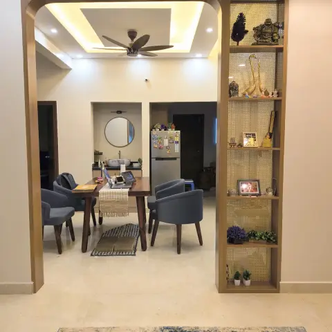 Wood-lined arch opening from a rug-laid living area into a dining table with blue tub chairs under a cove-lit POP ceiling and fan