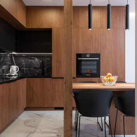 Wood-panelled kitchen with a black marble backsplash opens onto a dining table lit by three cylindrical black pendant lights