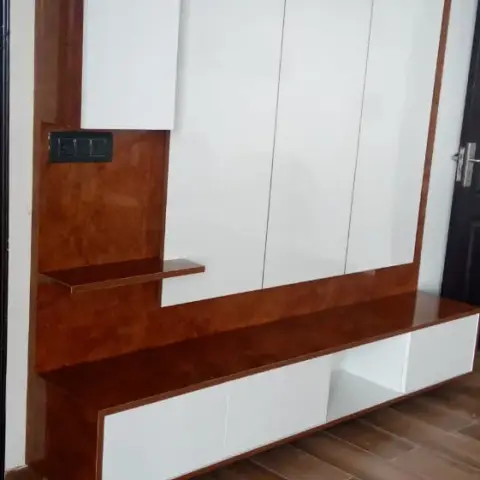 Wood-veneer and white gloss TV unit wall with an open display shelf and lower cabinets, no TV mounted yet, wood-look tile floor.