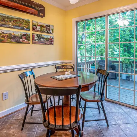 Yellow-walled breakfast nook with a round dark-wood pedestal table, chair-rail moulding, a gallery of folk-art paintings